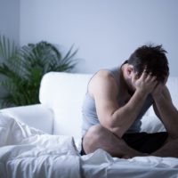 Man with depression sat on bed with head in his hands