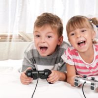 Young boy and girl lying on a bed enjoying playing video games together